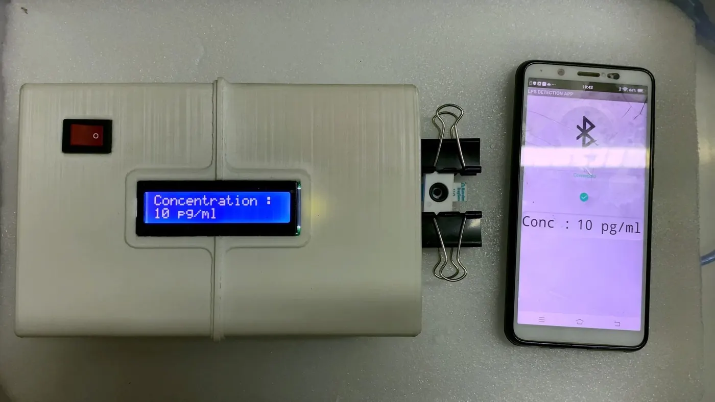 The Pratyasa research prototype: a white handheld analyser showing “Concentration: 10 pg/ml” beside an Android phone app reading the same value over Bluetooth.